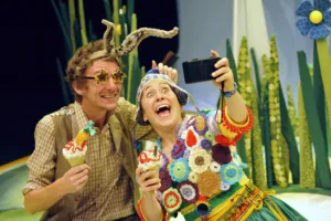 Two actors on stage in colorful outfits taking a selfie together