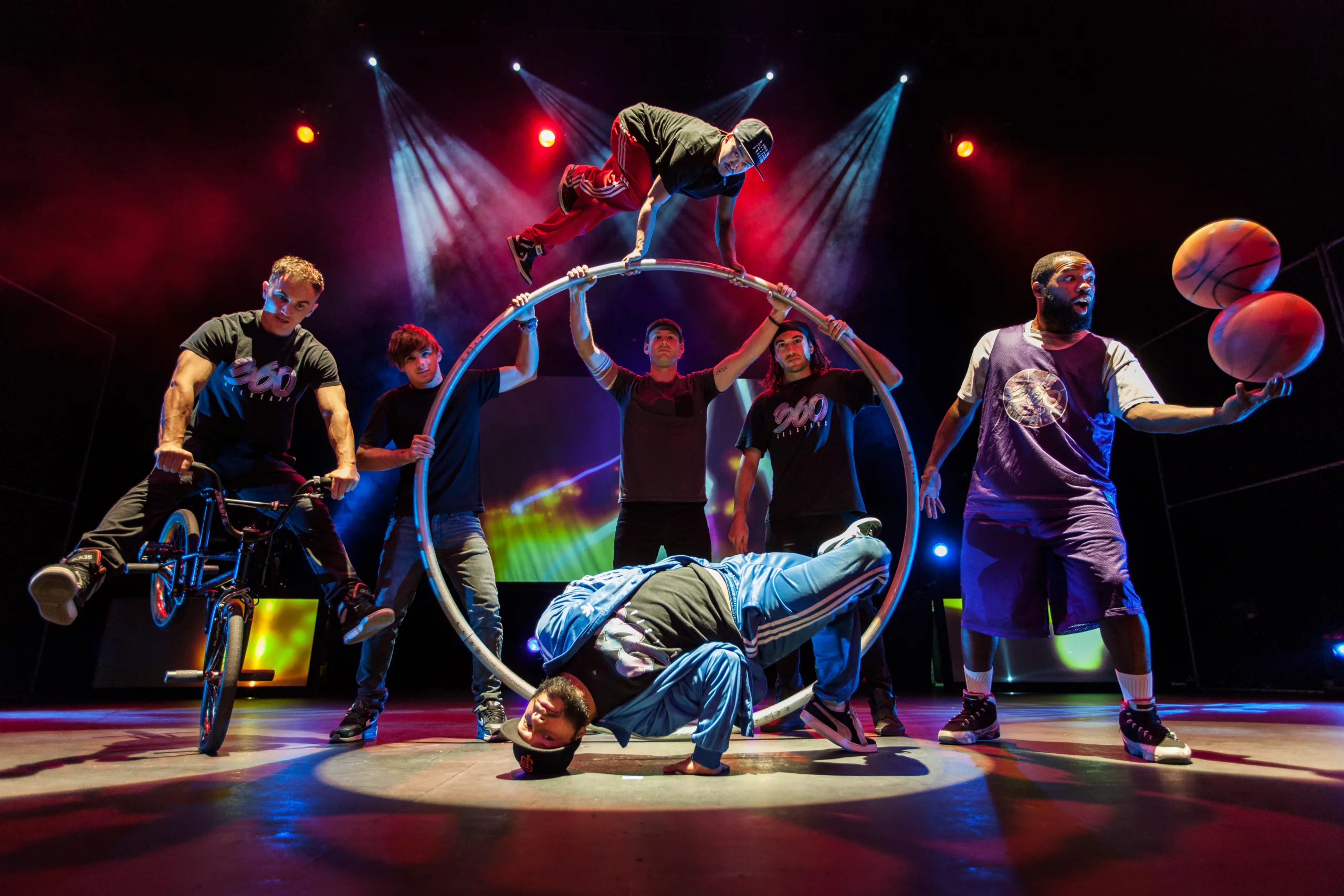 360 ALLSTARS pose on stage with basketballs, BMX bike and acrobatic circle on stage.