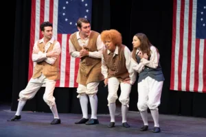 Four actors on stage in colonial costumes