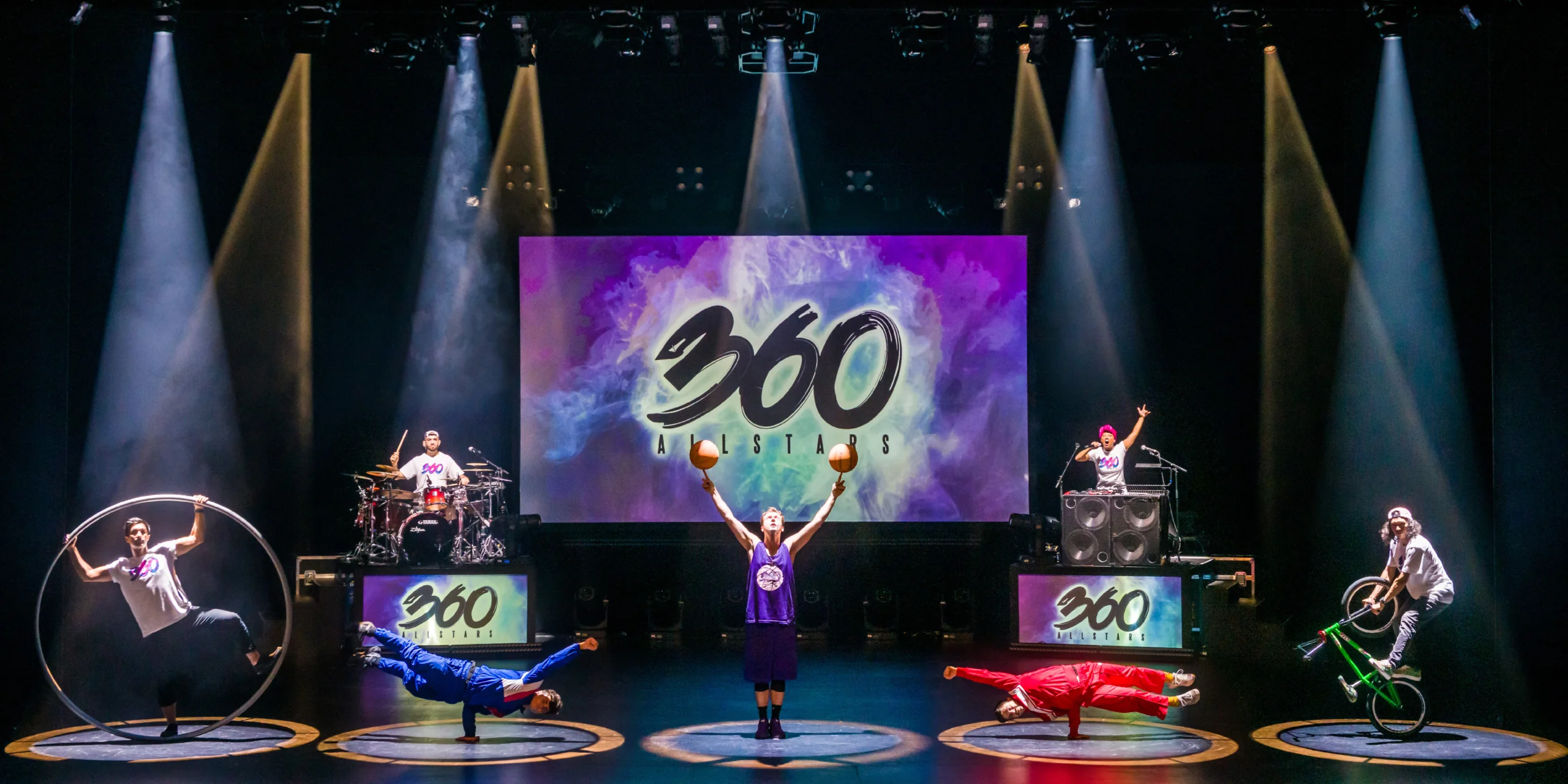 360 Allstars posing with BMX bike, basketball, breakdancing, beatboxing, acrobatics, and drumming on stage.