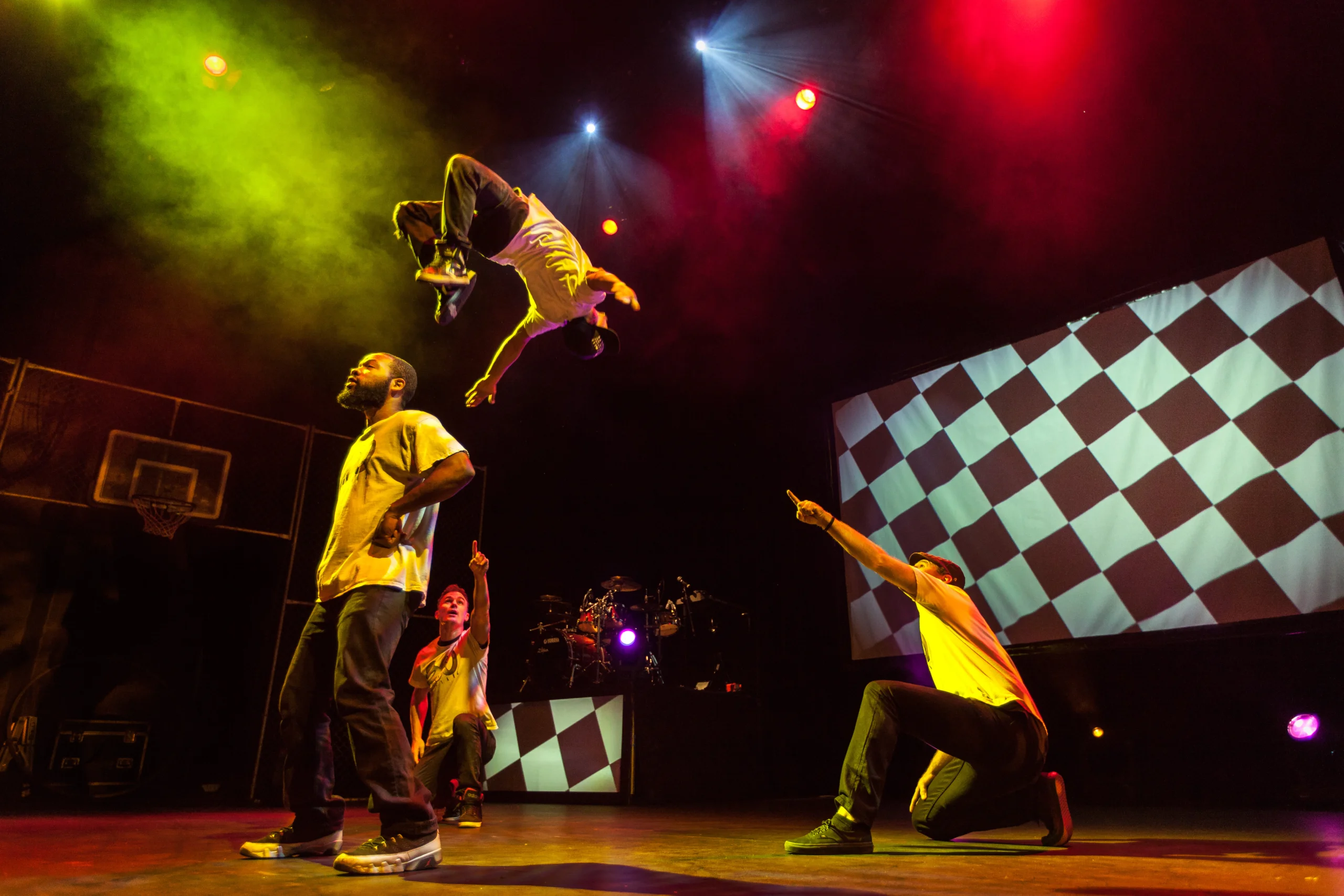 Guy doing a backlip of another person while pointing at jumper on stage.