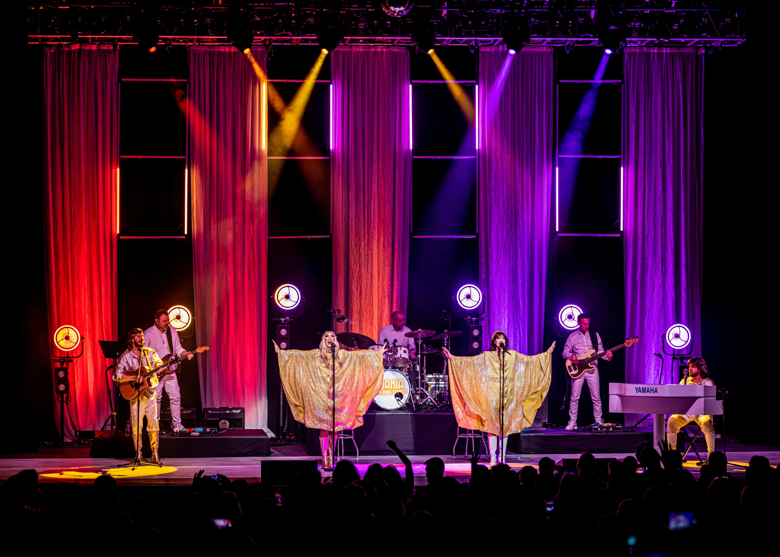 Four members of Mania on stage in ABBA costumes in bright colourful lights.