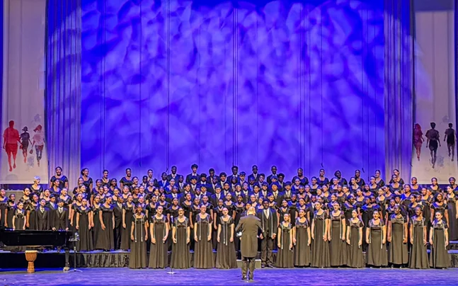 Young Singers choir wearing black on stage singing in front of a blue background.