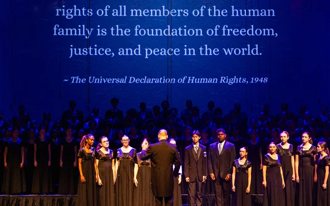 Young Singers choir wearing black on stage singing standing in front of the Universal Declaration of Human Rights, 1948.