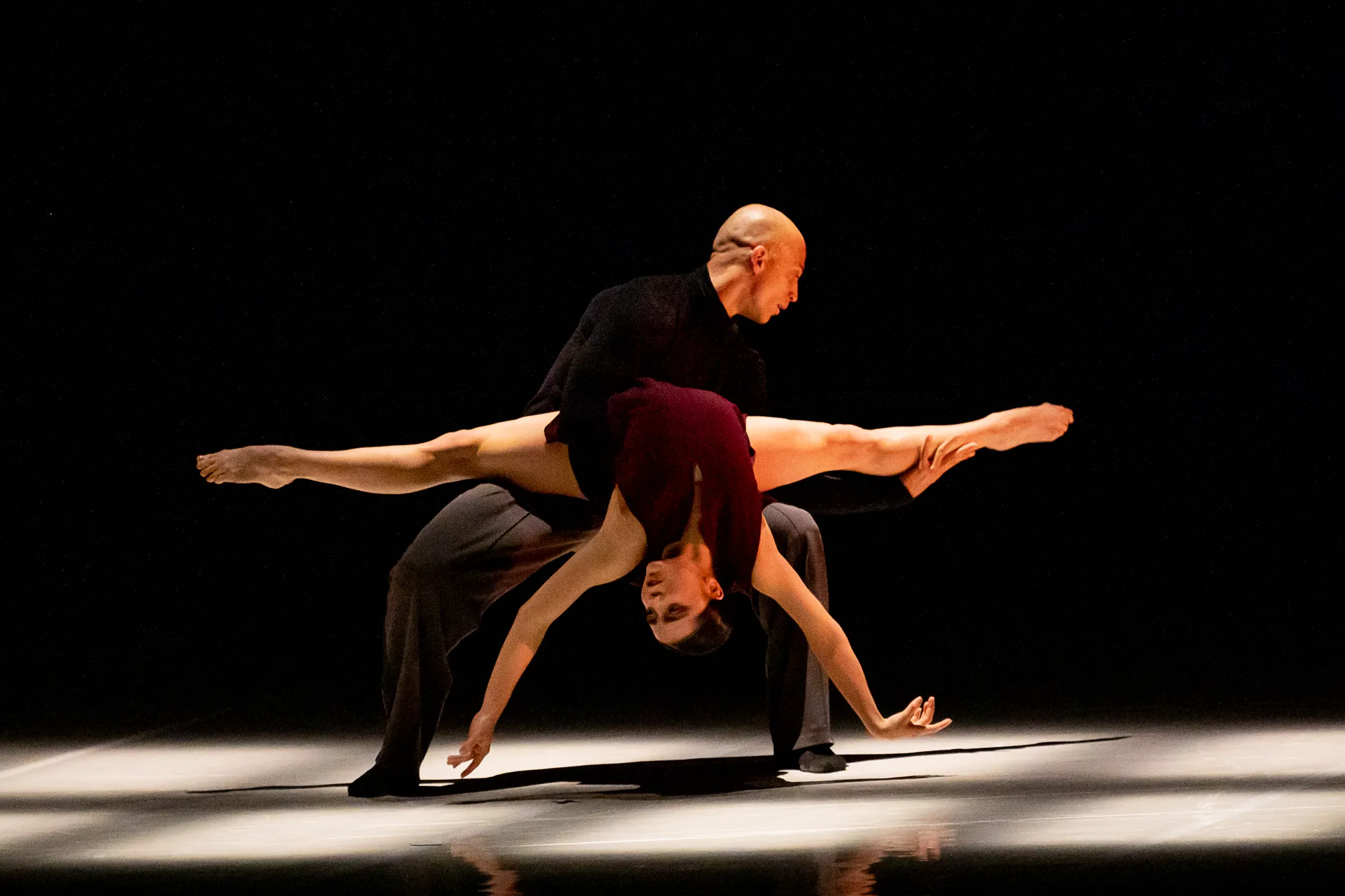 Ballerina held upside down in a red dress and a man in black balancing her.