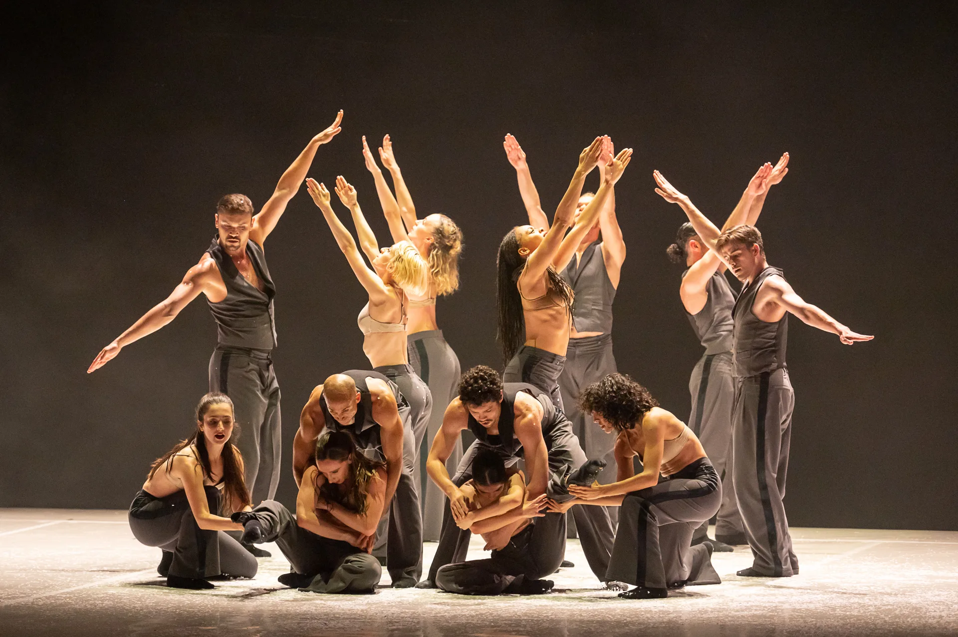 The ballet company in black and gold posing some crouching and some with their arms extended.