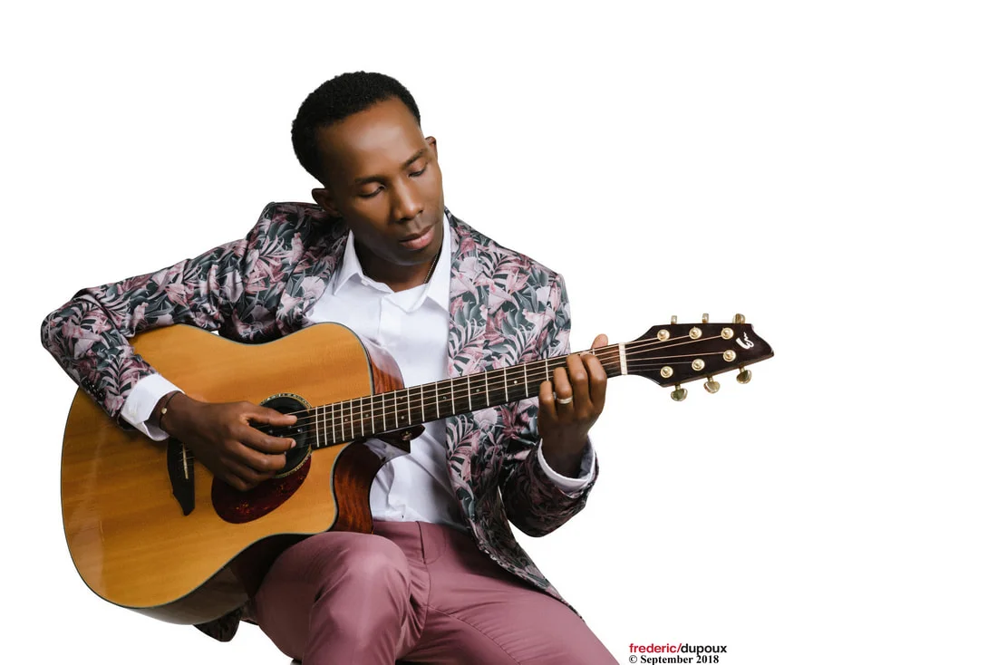 BélO siting on stool playing guitar.
