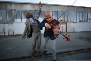One man dancing in a suit while the other plays the vioin