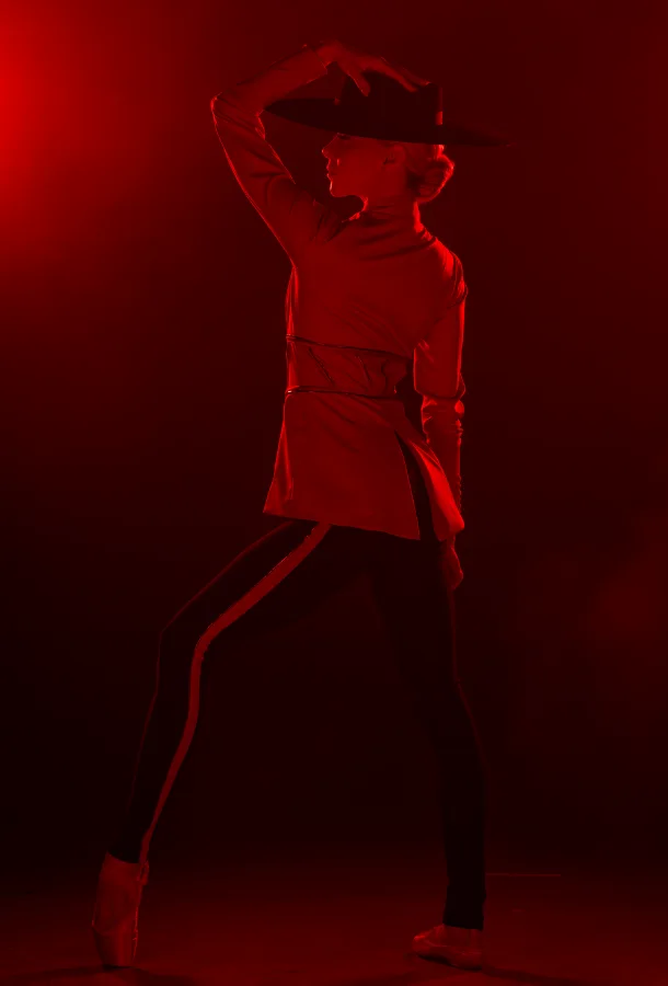Ballerina bathed in red hazy light posing with a fedora on her head.