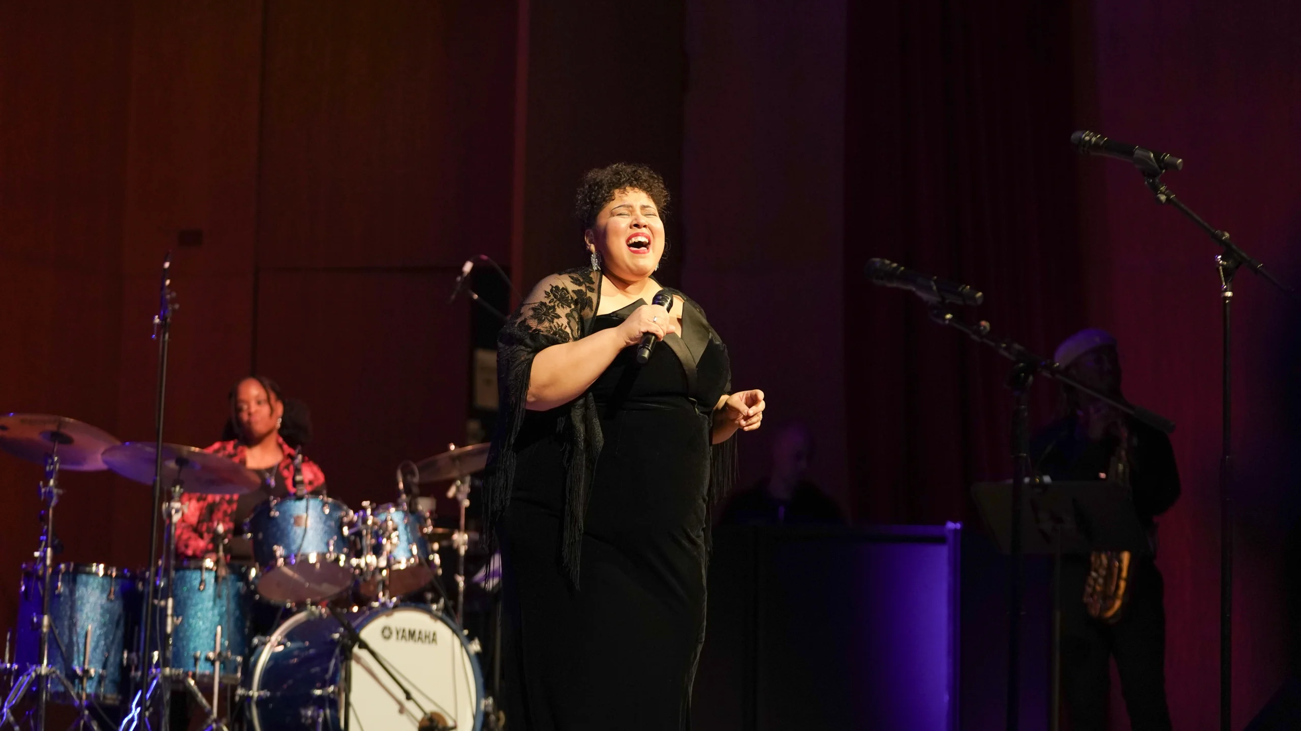 women belting out a song with microphone on stage.