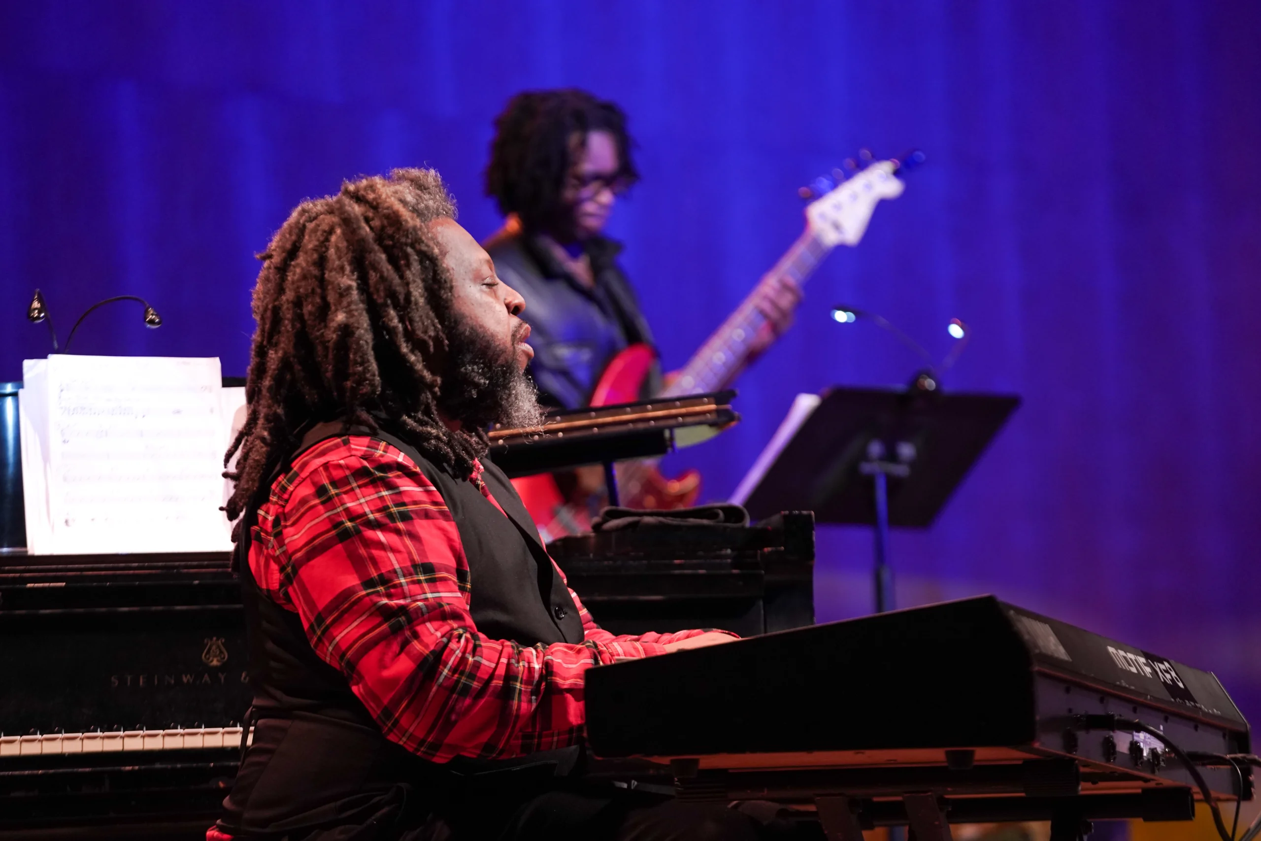 man playing at keyboard and man on guitar playing in the rear.
