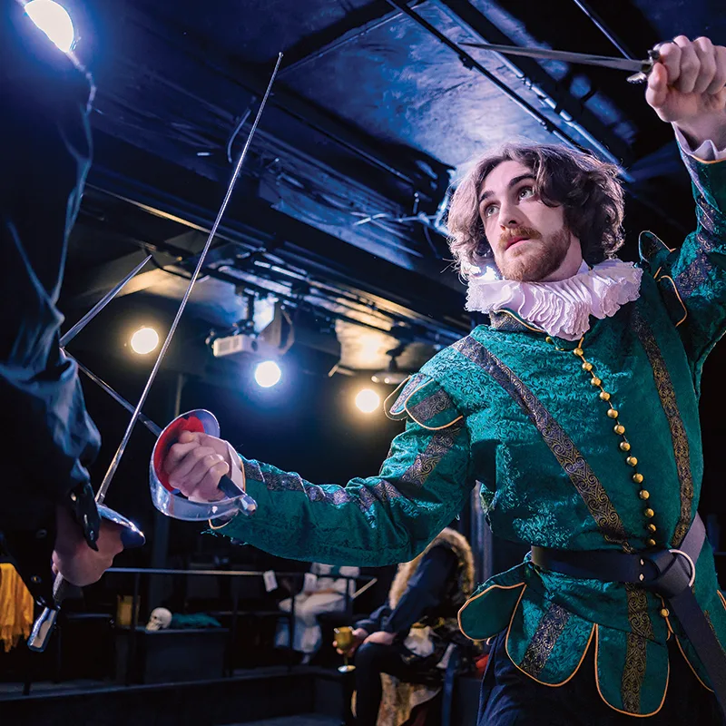 Man in Elizabethan costume holding a dagger and sword about to spar.