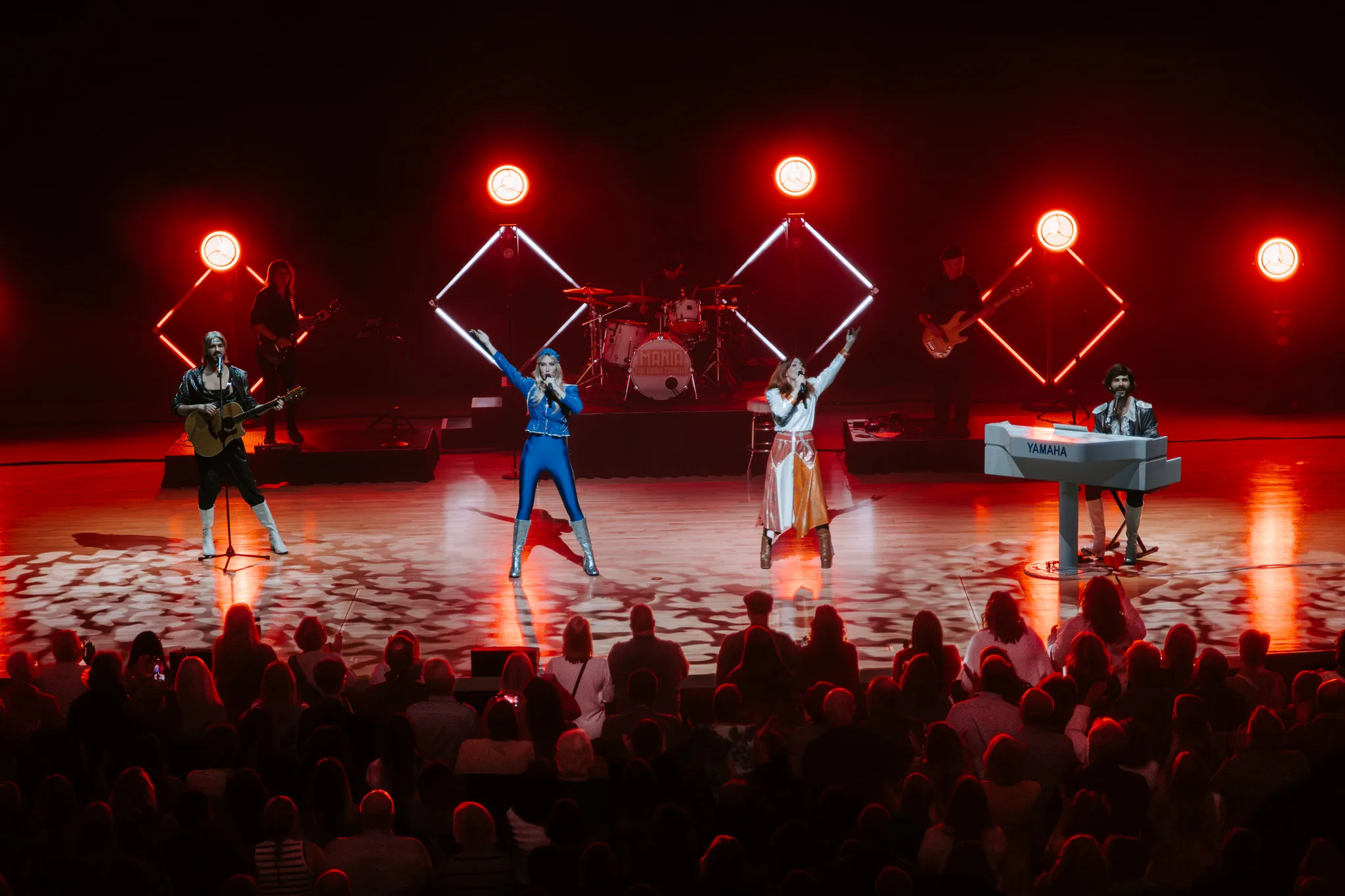 Four members of Mania on stage in ABBA costumes in bright colourful lights.