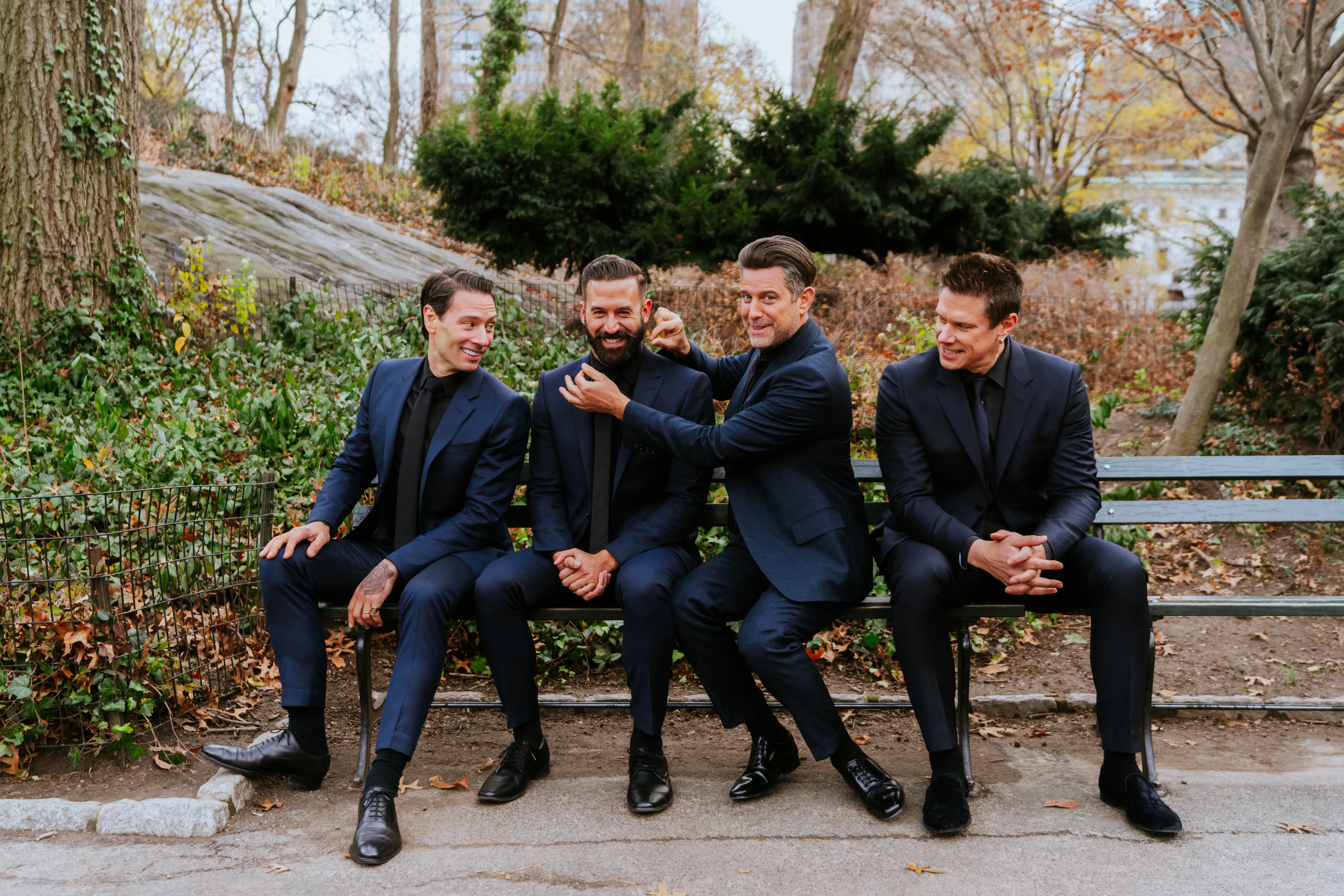Four members of Il Divo in black sitting on a bench together.
