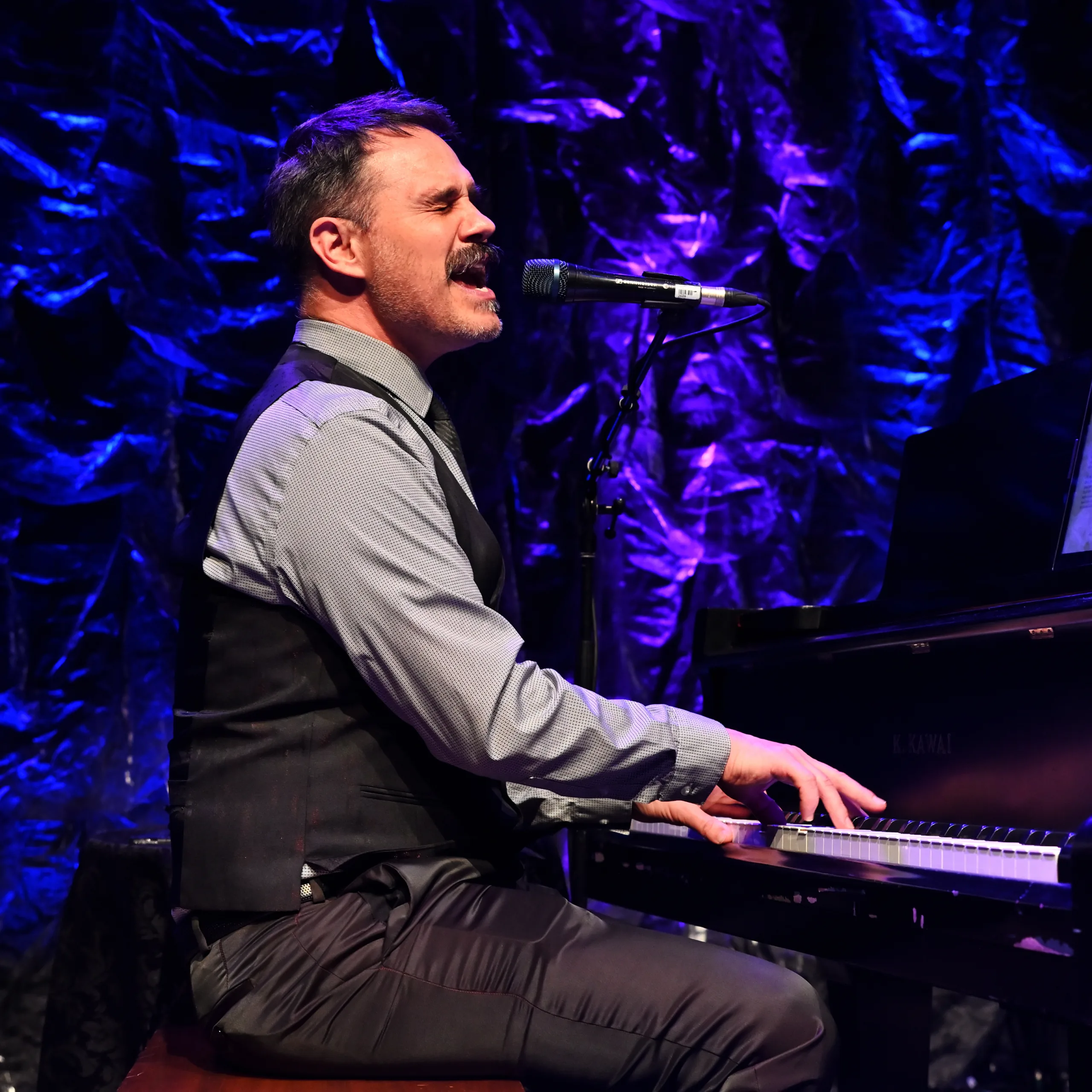 Joel Parisien singing into a microphone at a grand piano.