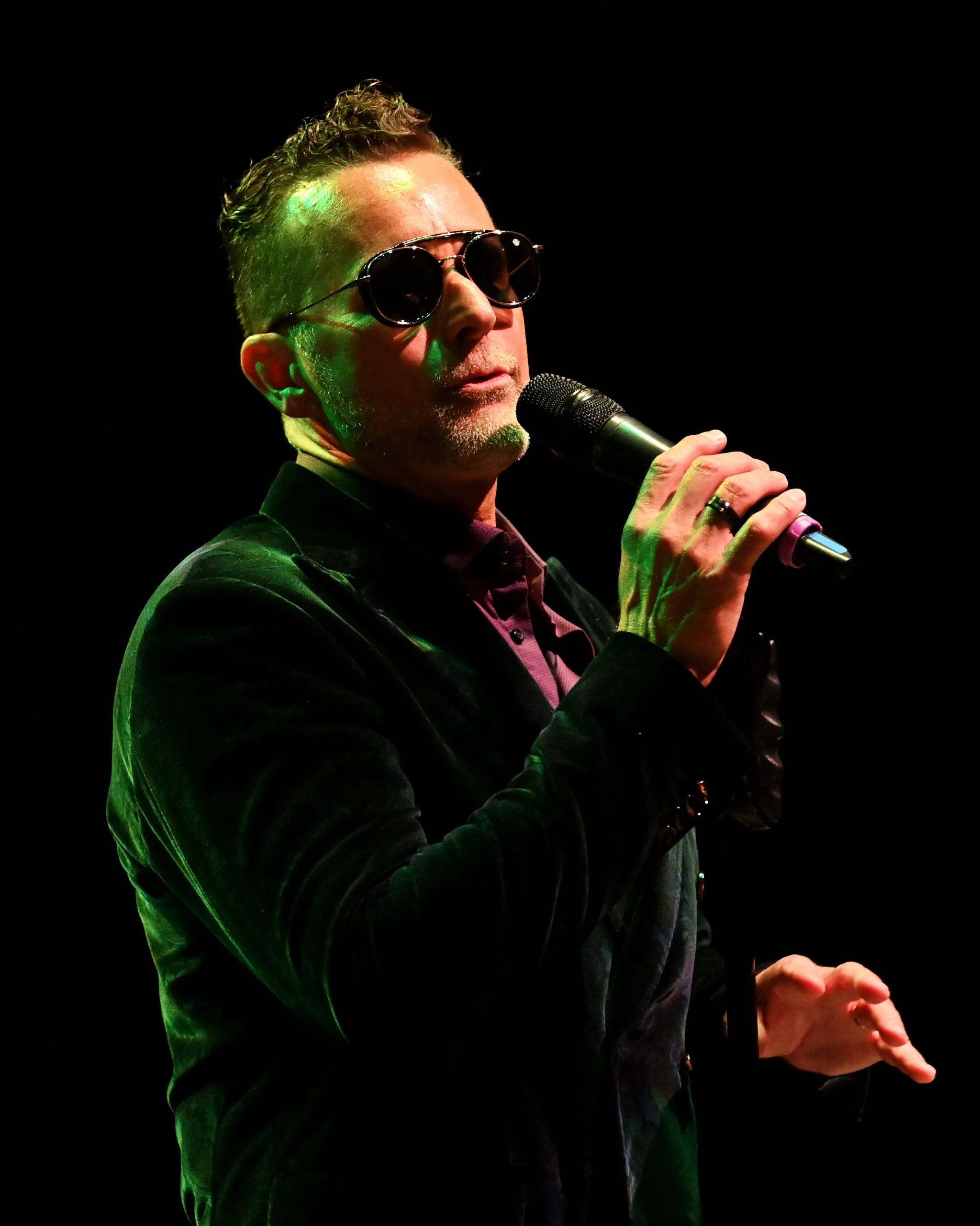 Kevin Pauls singing into a microphone wearing a green velvet blazer.