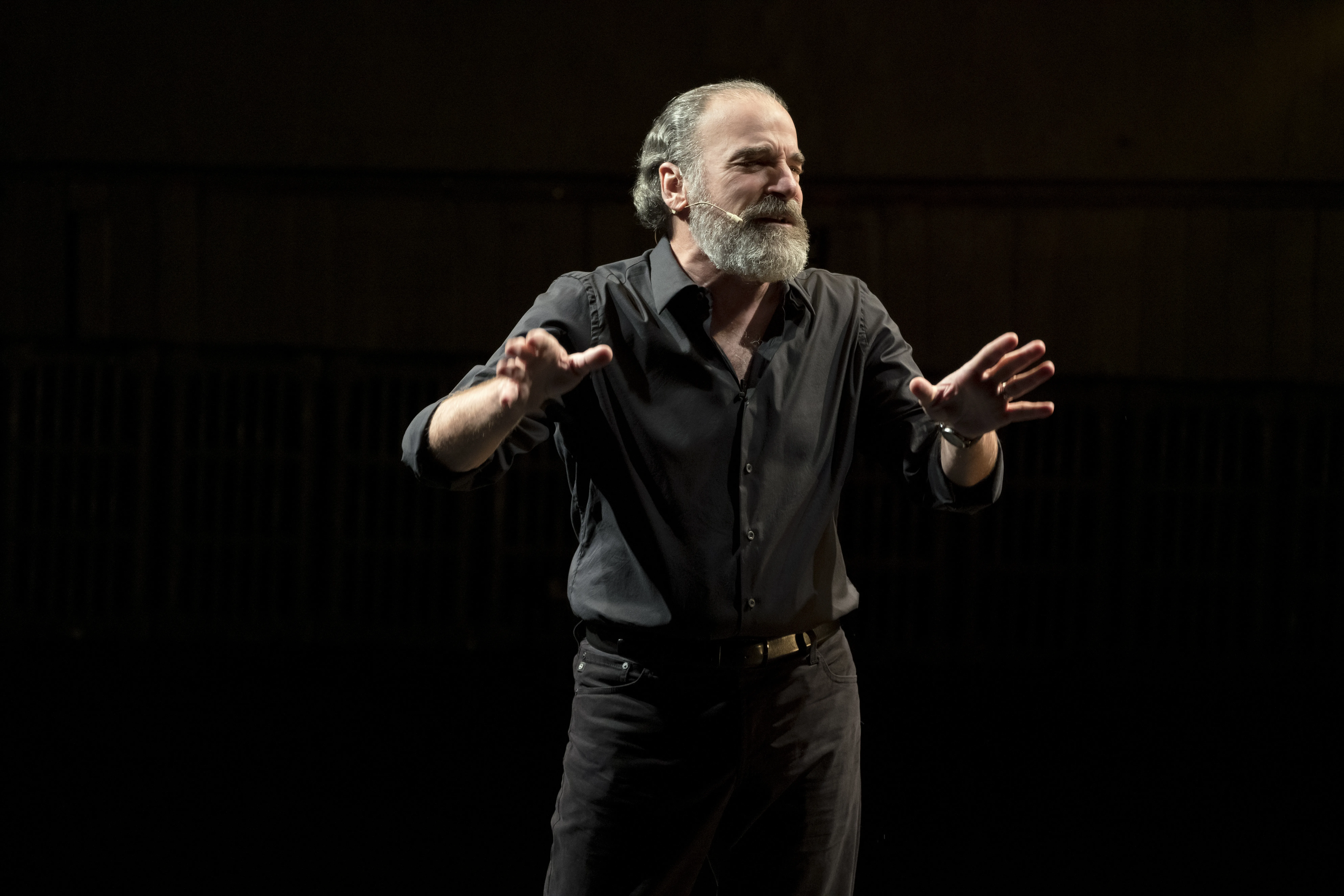 Mandy Patinkin gesturing on stage wearing black.