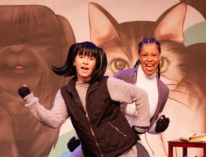 2 actresses on stage dancing behind each other.