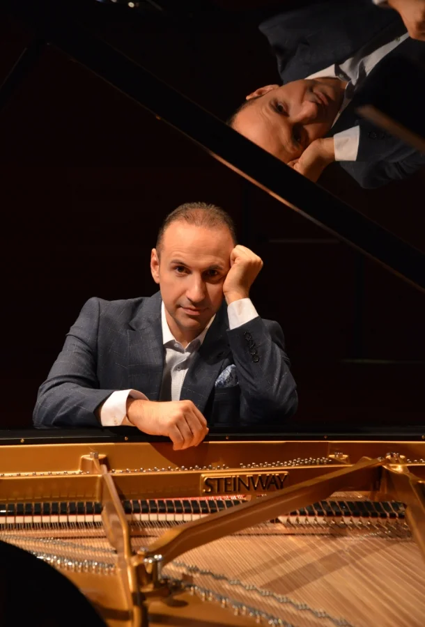 Simon Trpčeski headshot with an open piano looking toward camera.