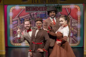 Actors on stage smiling in brown reindeer-like outfits