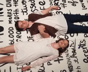 Romeo & Juliet lying down with words written beneath them like a canvas.