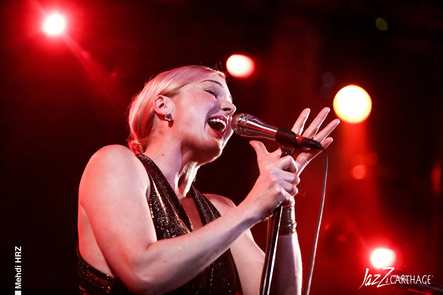 Woman singing passionately into a microphone with red lights in the background.