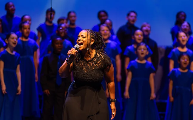Young Singers choir wearing black on stage singing with one lead singer singing into a microphone.
