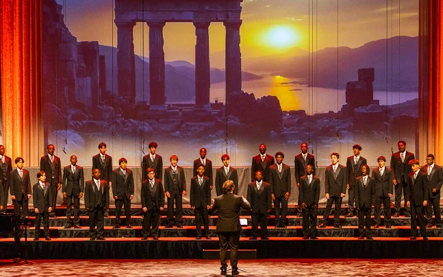 Young Singers choir wearing black on stage singing with a setting sun back drop.