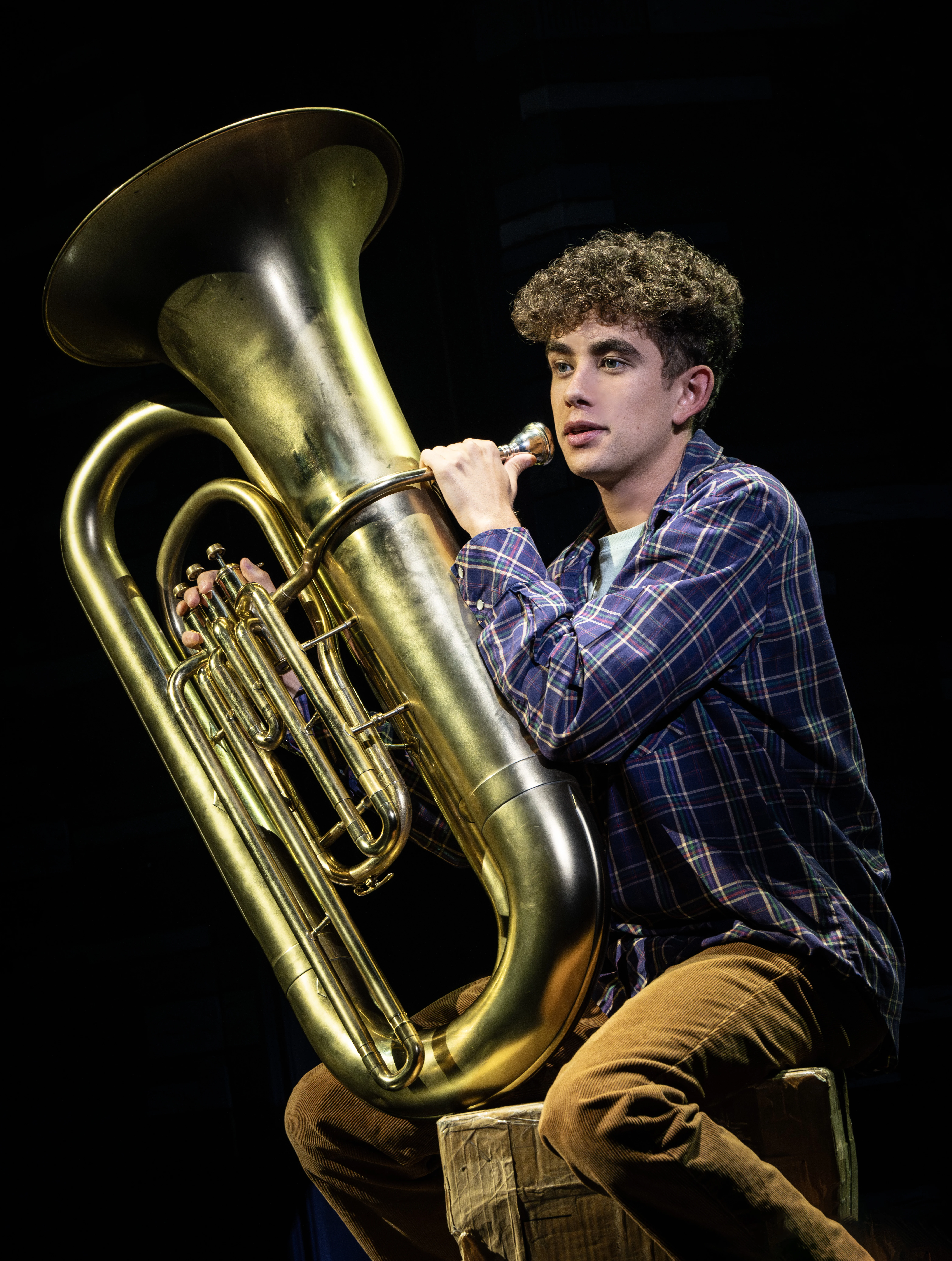 Teenage boy sitting on a cardboard box holding a tuba.