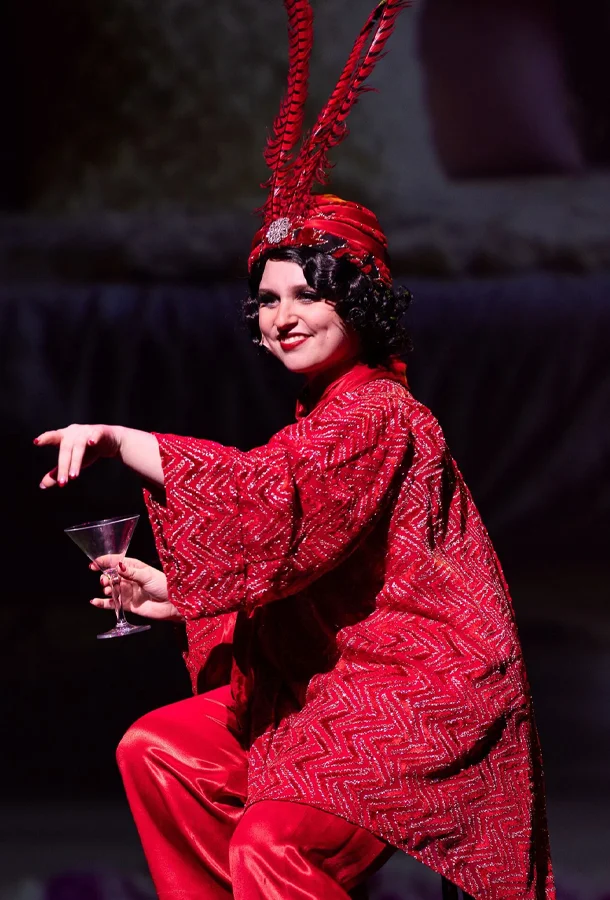 JJ Korkin wearing a red robe and a red feathered hat pointing down toward the audience.