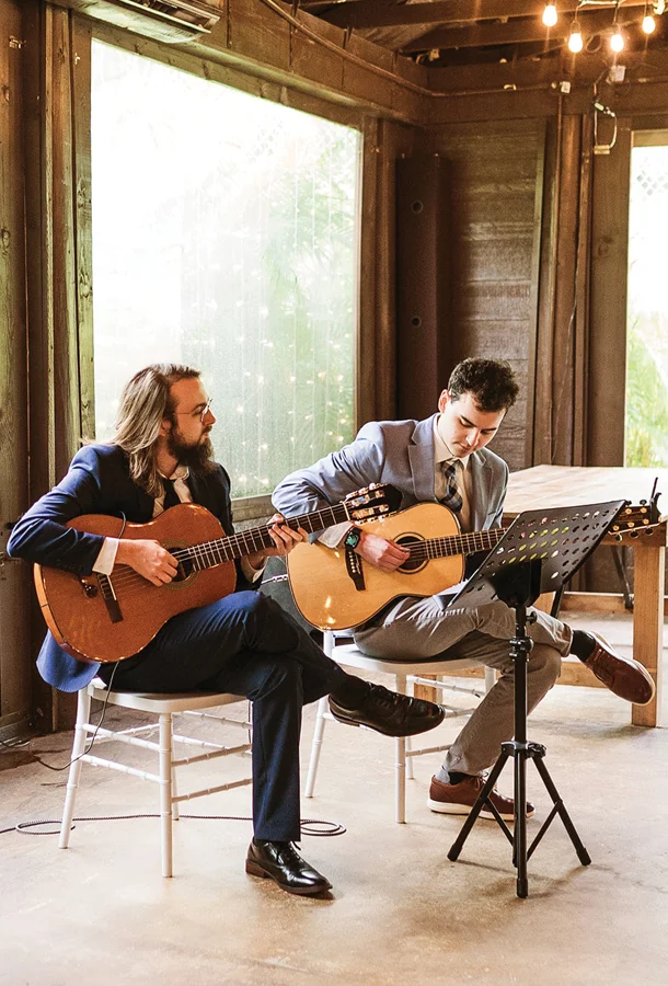 Two men wearing suits playing acoustic guitar