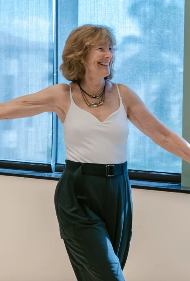 Woman wearing a white tank top with her arms out.