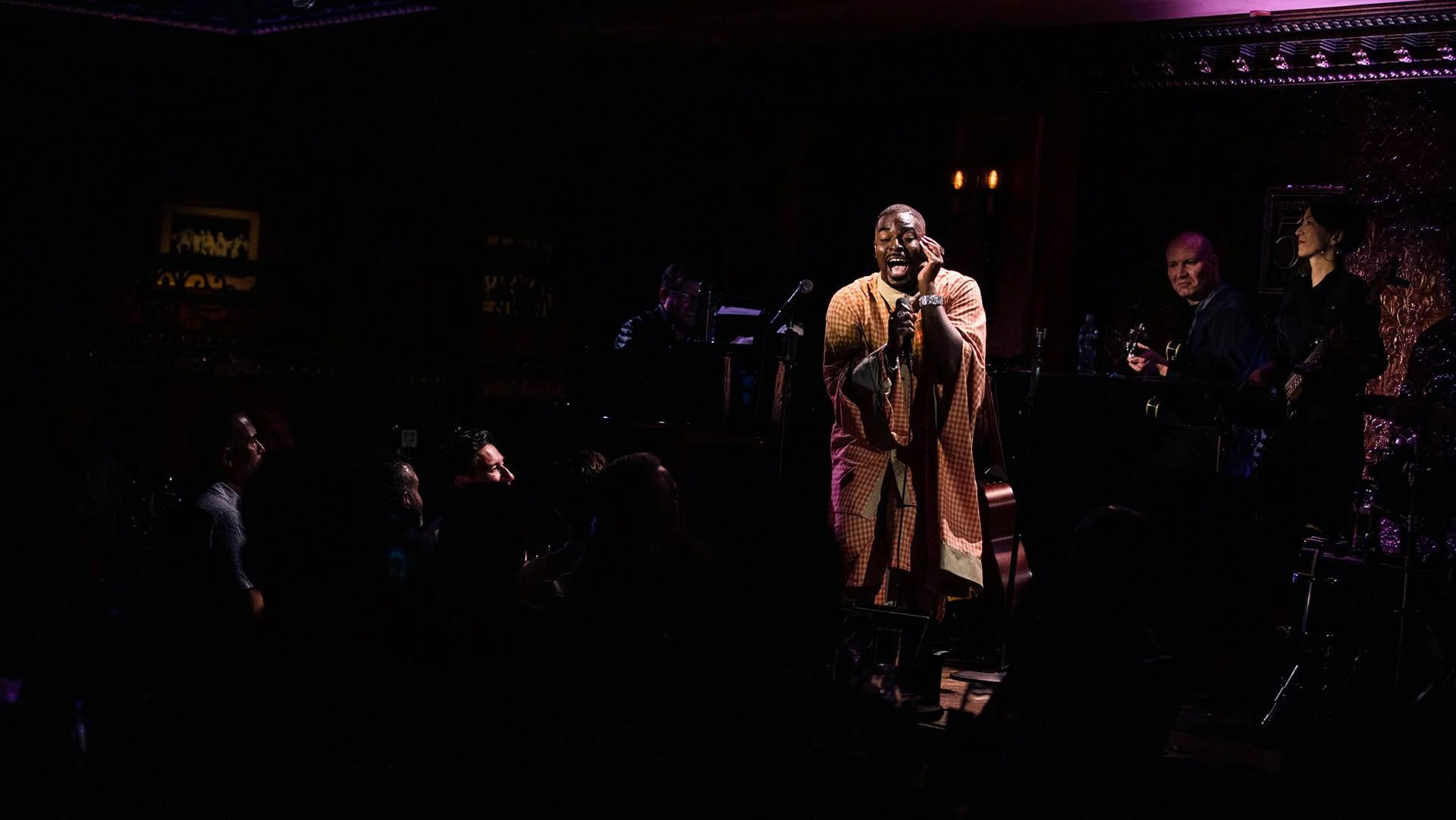 Kyle Taylor Parker wearing a orange outfit singing on a dark stage.