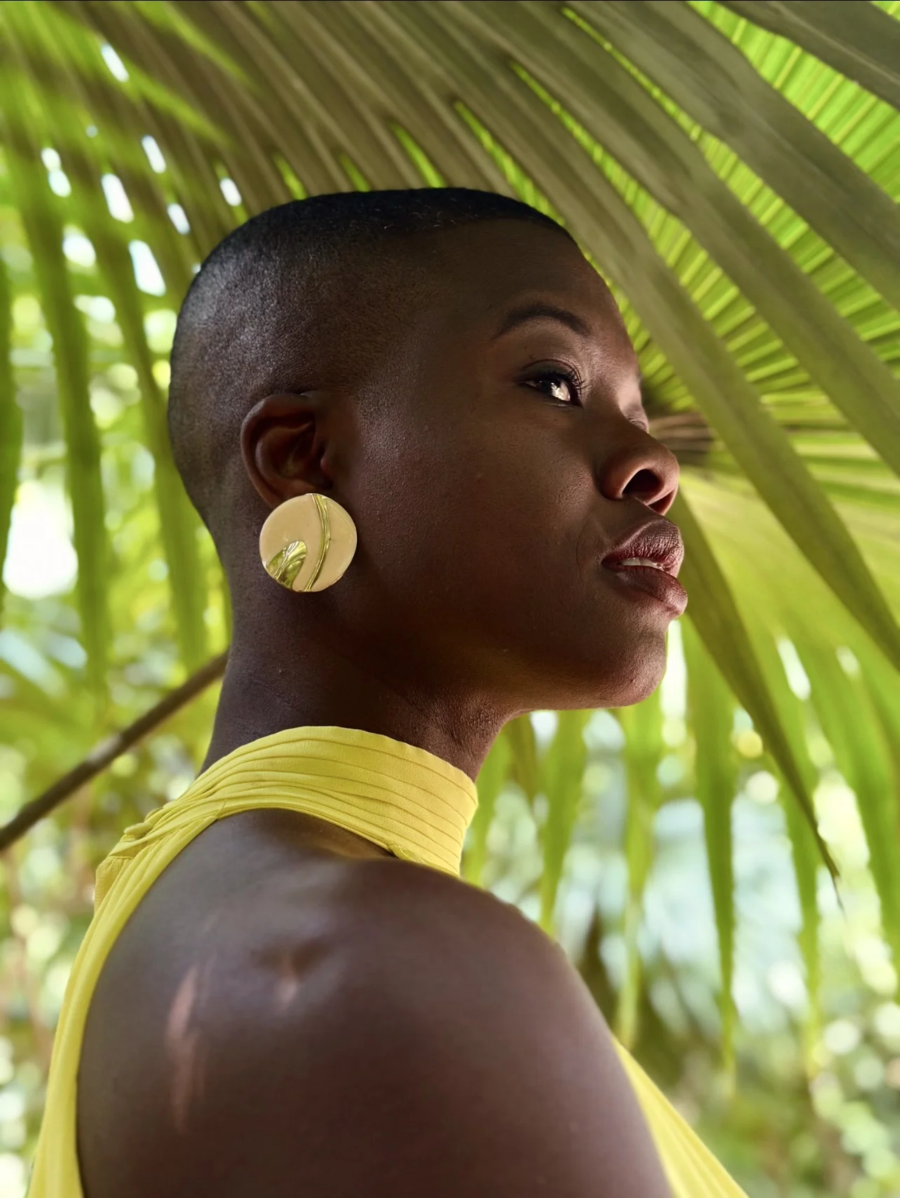 Nadege Gren wearing yellow standing in front of palm fronds.