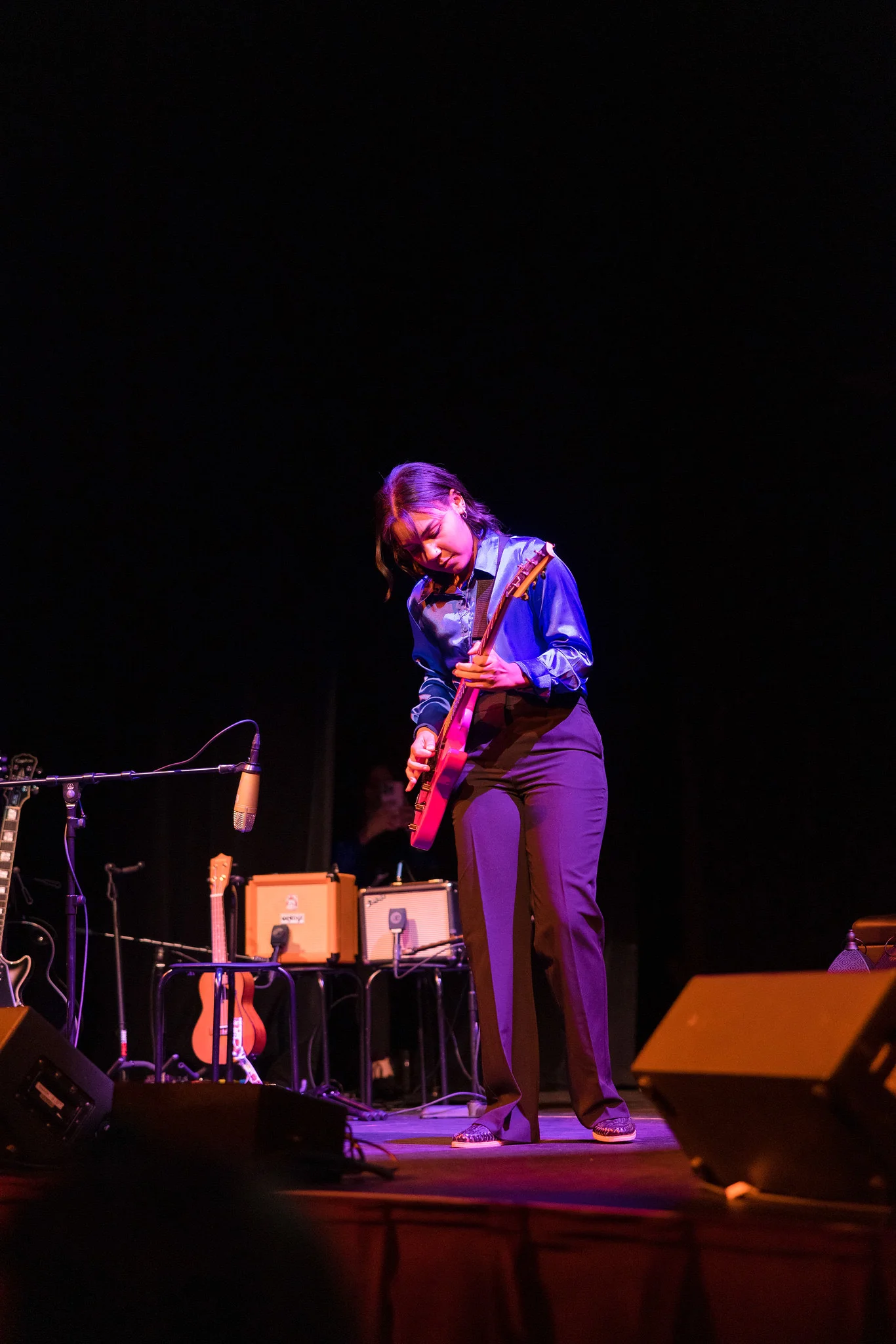 Young female student playing guitar on dim lit stage.