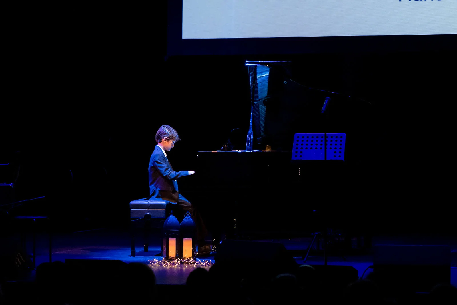 Young student playing piano on dark lit stage.