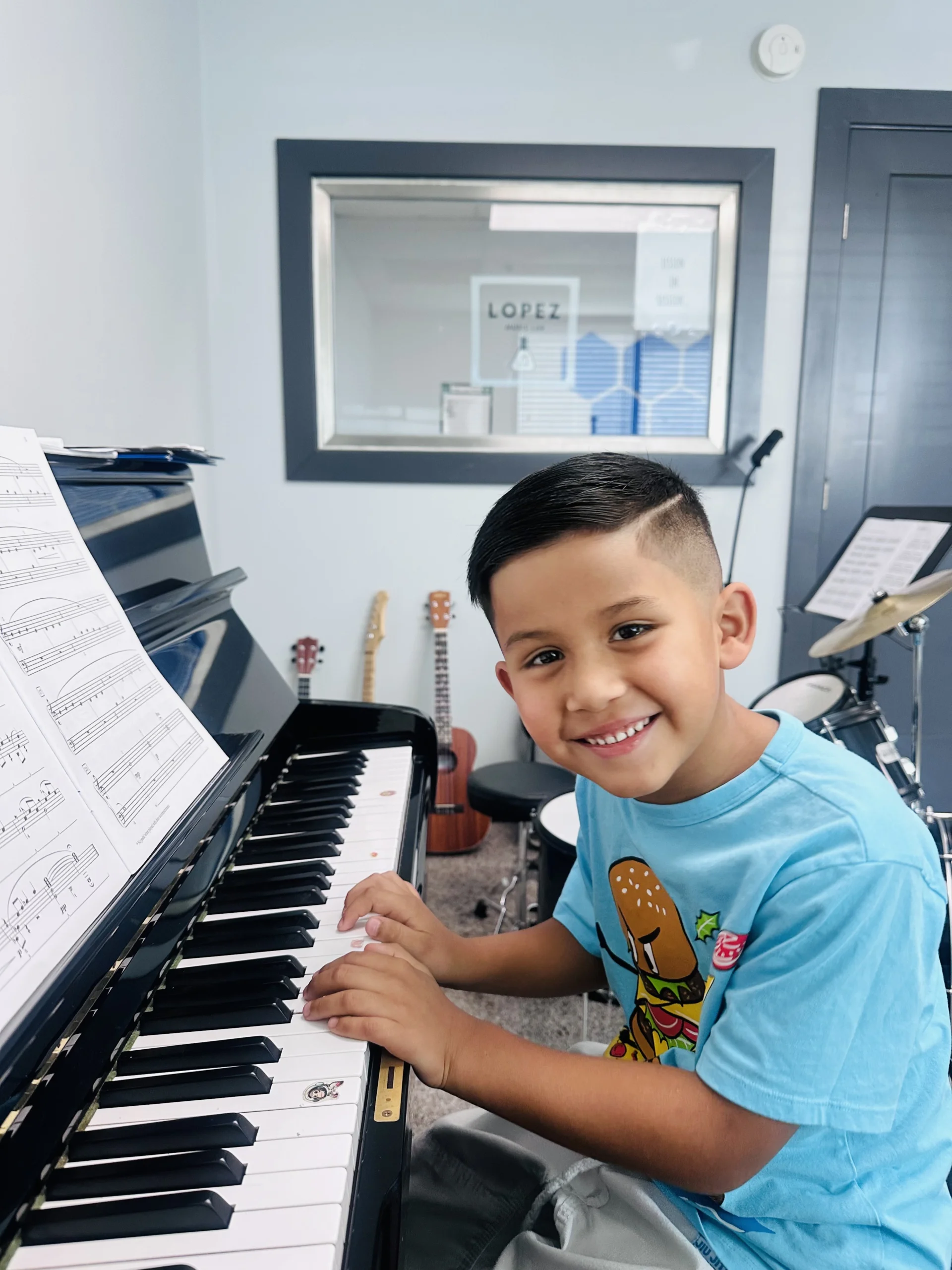 Young student smiling at camera while posing at piano in music studio.