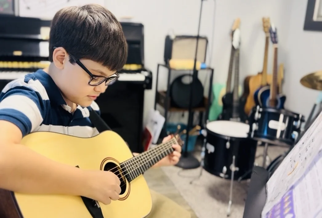 Young student playing guitar in music studio.