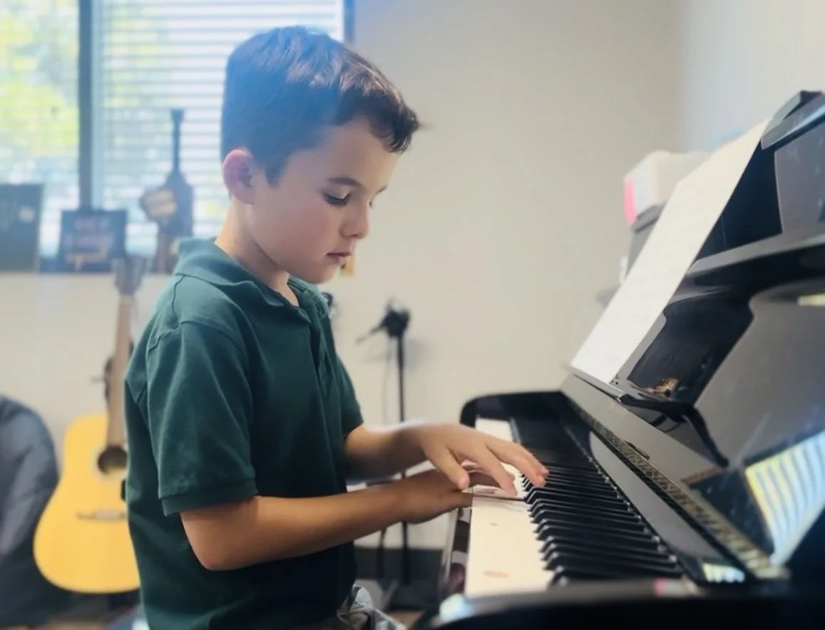 Young student wearing green shirt playing piano in music studio.