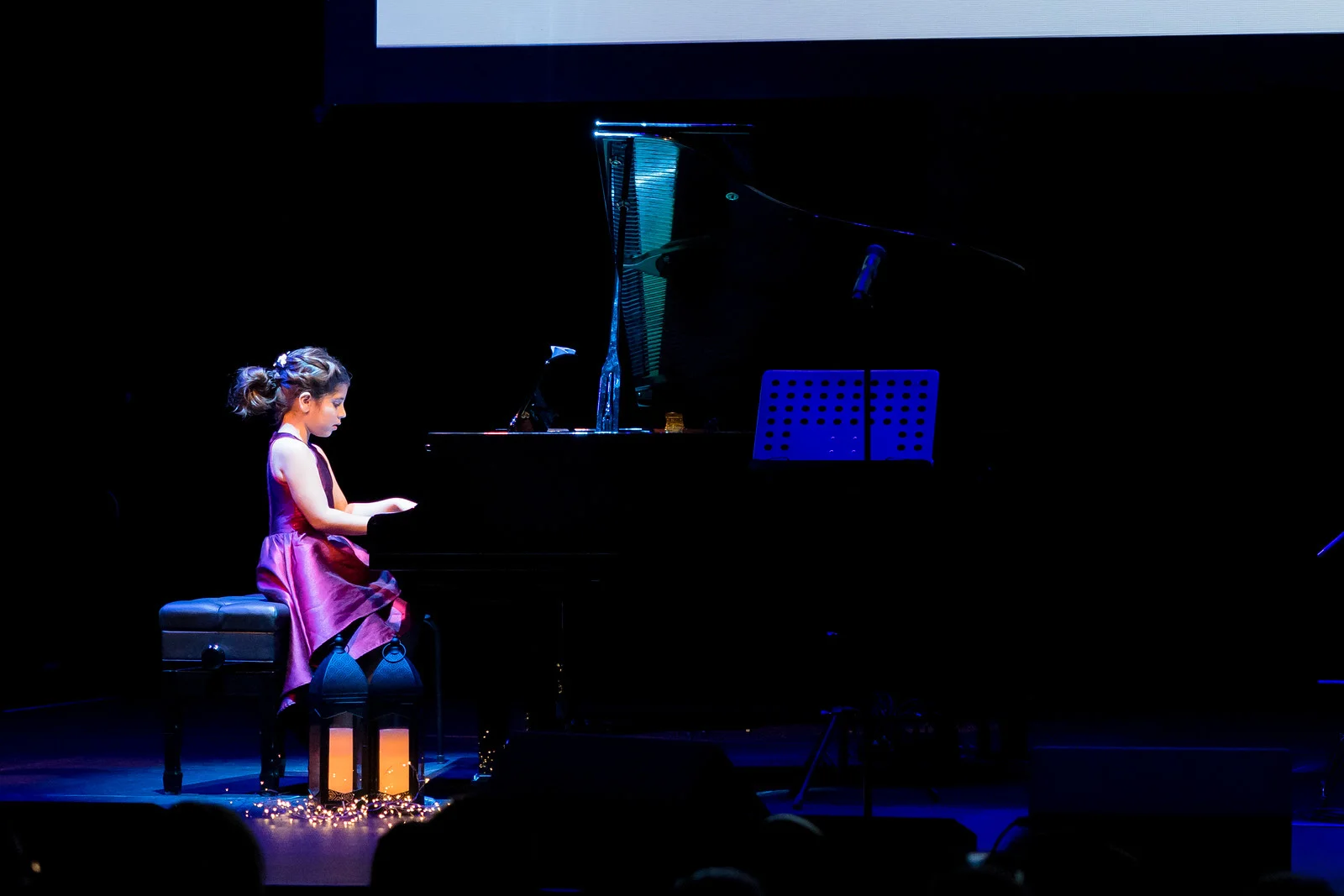 Young female student playing piano on dark lit stage.	