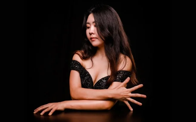 Chloe Jiyeong Mun wearing a black dress with her arms crossed and fingers splayed. 