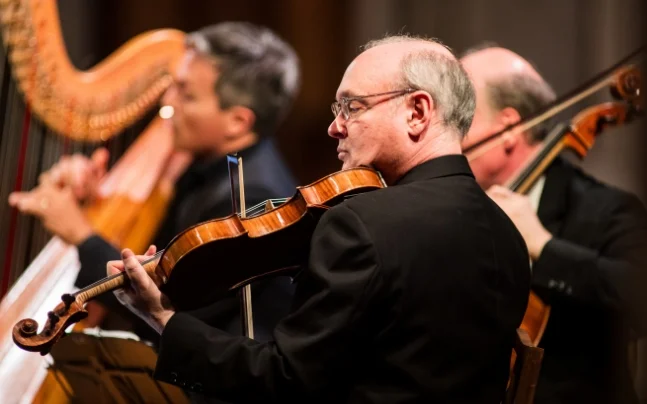 Paul Neubauer playing viola with the rest of the orchestra in the background. 