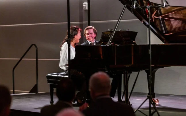 Double Forte Chamber Music Society of Palm Beach Juho Pohjonen and Wu Qian sitting at a piano smiling to each other on stage.