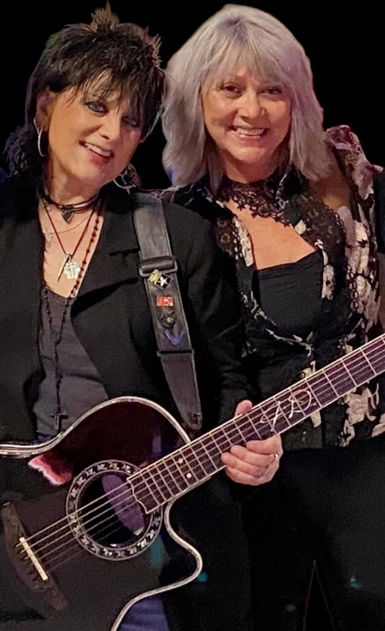 Two females pose for camera while holding guitar