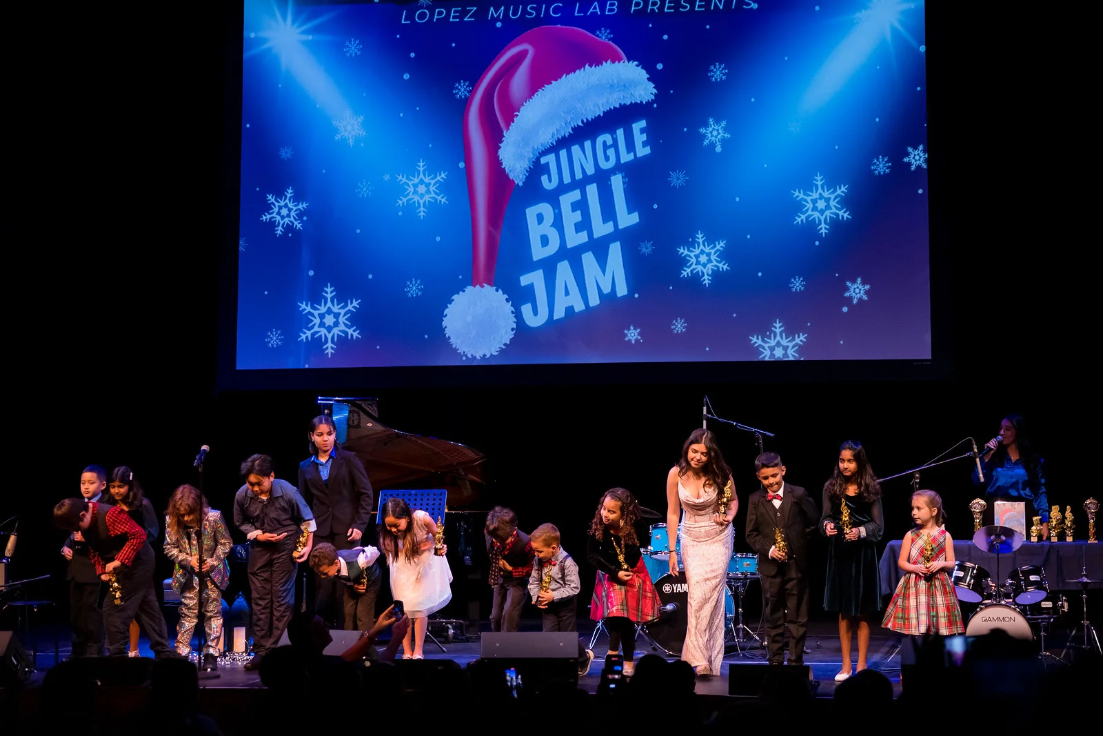Young students and teachers bow on stage.