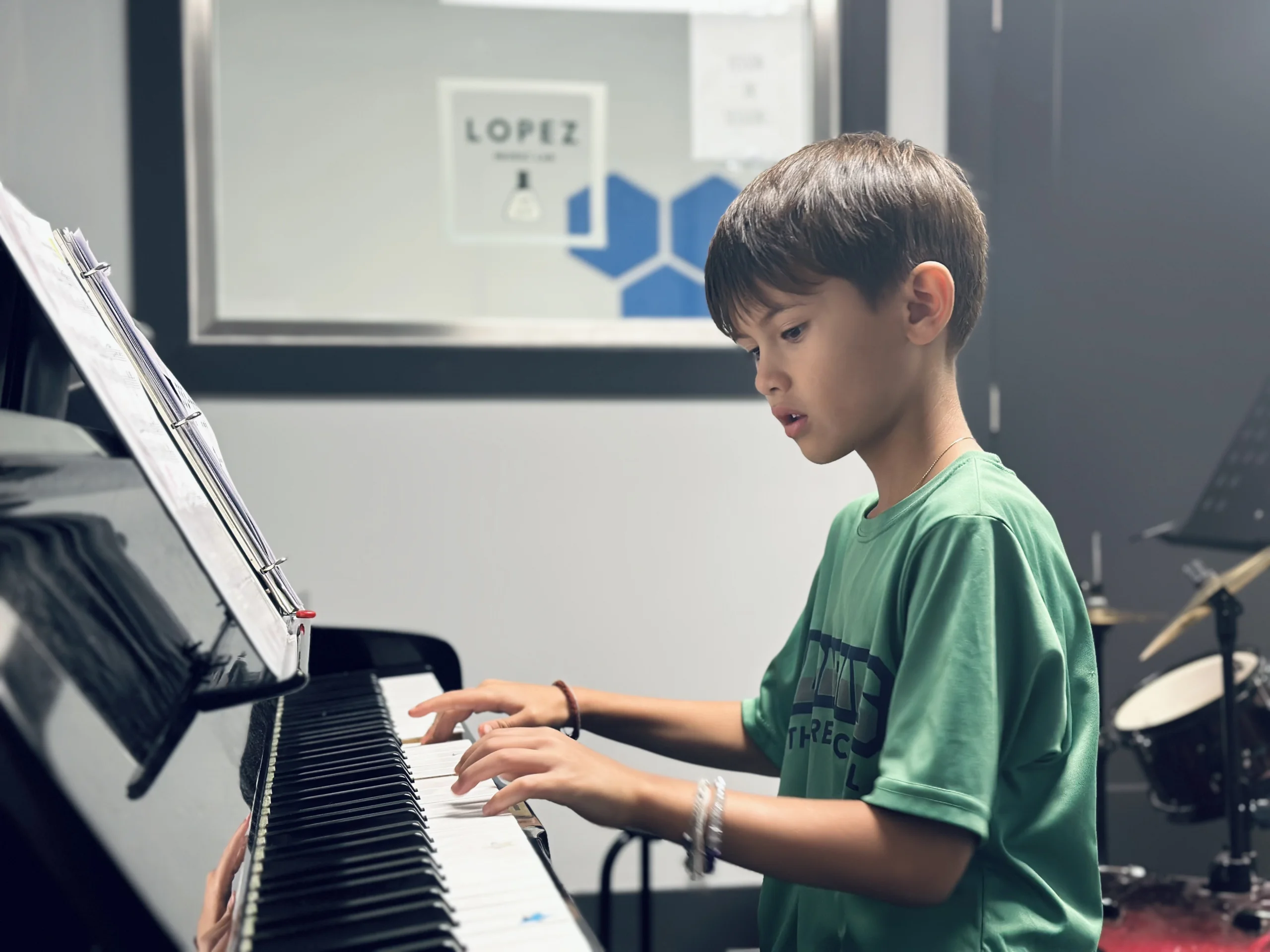 Young student wearing green shirt playing piano in music studio.