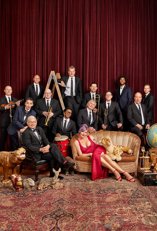 Pink Martini group photo around a couch with Storm Large siting with plush tiger.