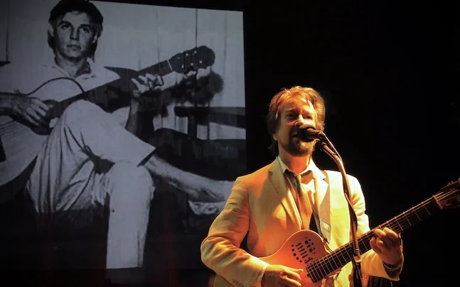 man on stage playing and singing guitar.