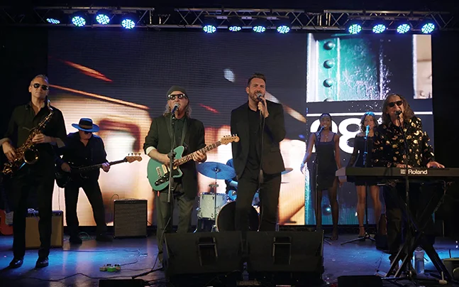 The Expanding Man perform on stage with backup singers.