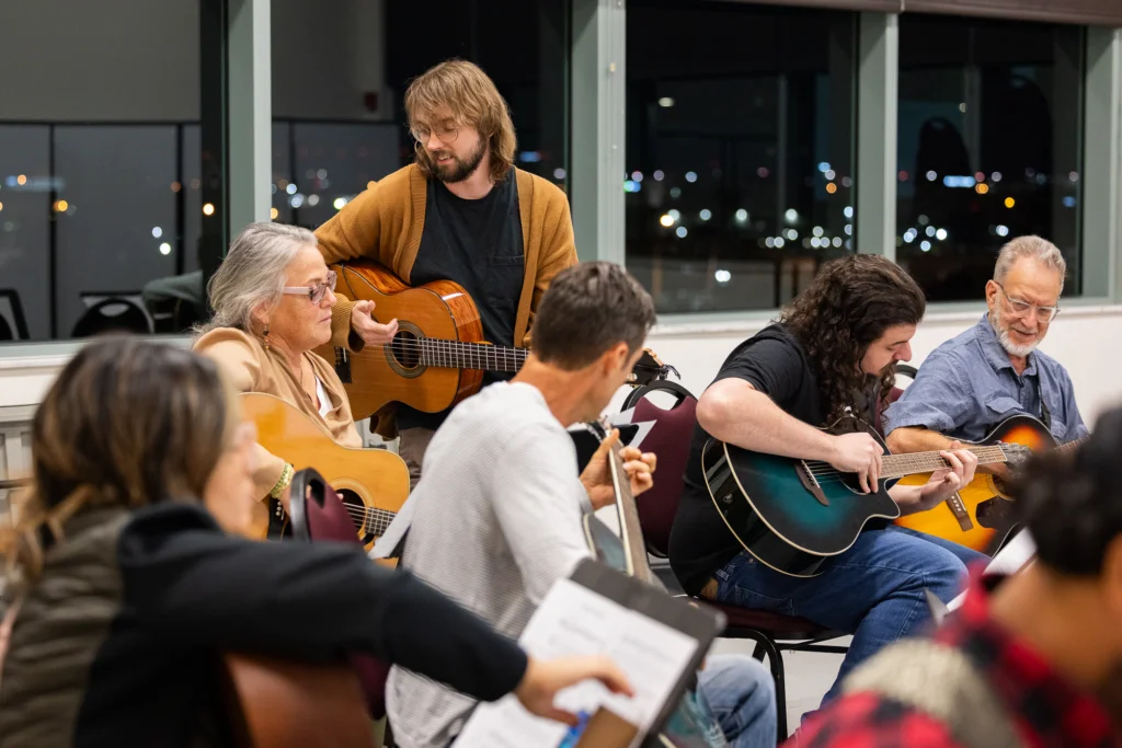 Guitarist teaching a guitar class to a group of adults.